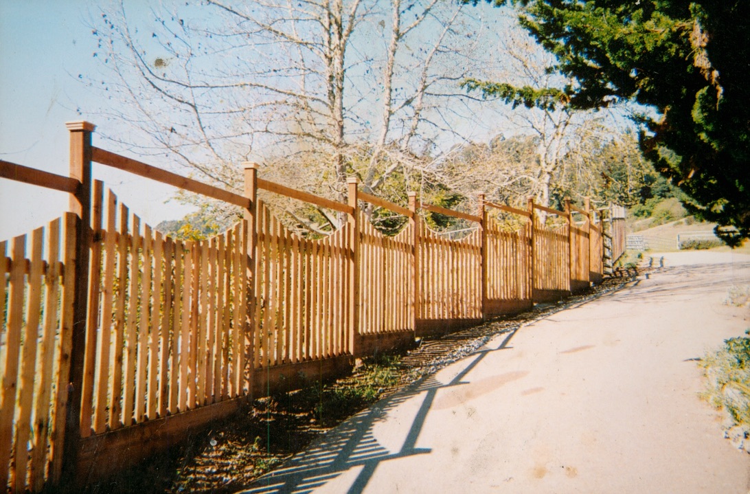 Wood picket-style fence installation along a sidewalk, creating a defined boundary with a natural decorative look.