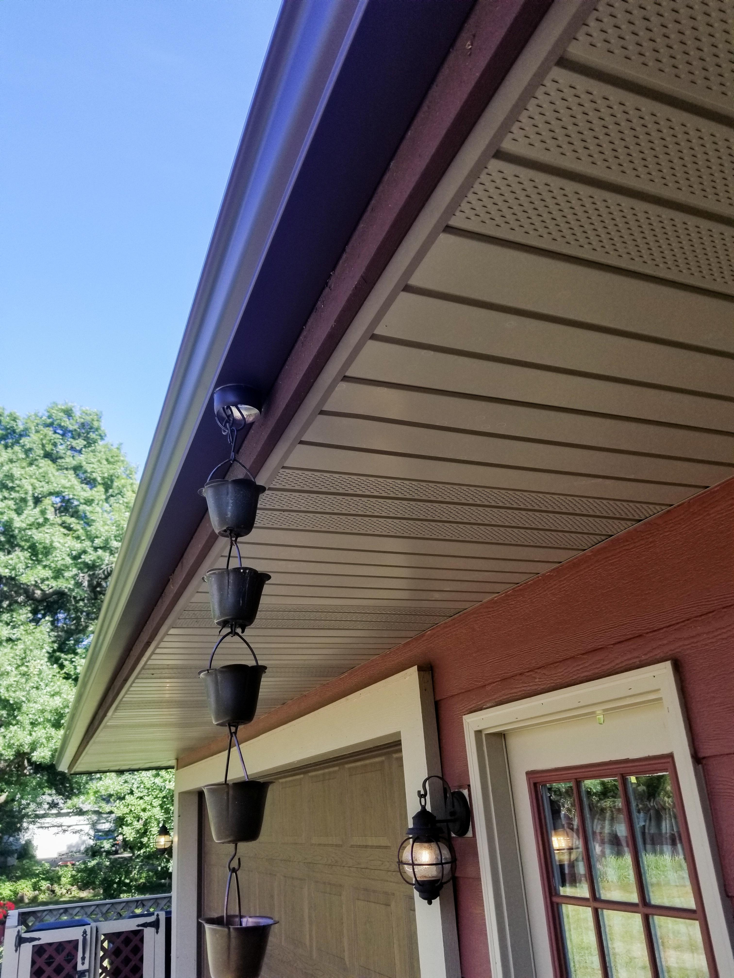 Dark seamless gutter featuring a decorative metal bucket rain chain installed on a red home by Ultimate Gutter Solutions.