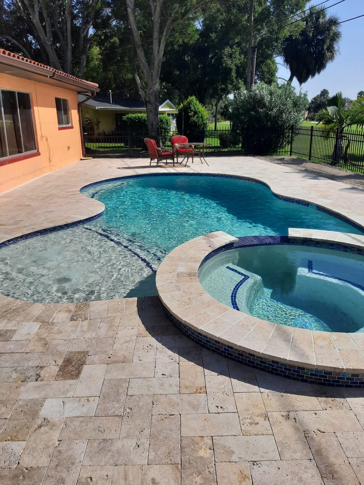Freeform backyard swimming pool with an attached round spa, curved stone coping, paver decking, and tropical landscaping.