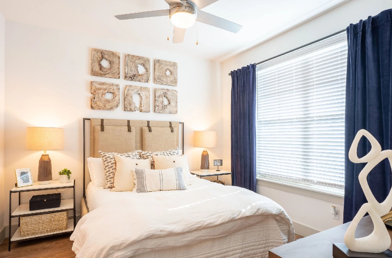 Furnished bedroom at The Drake Apartments in Midland, TX with a ceiling fan, navy curtains, and warm 