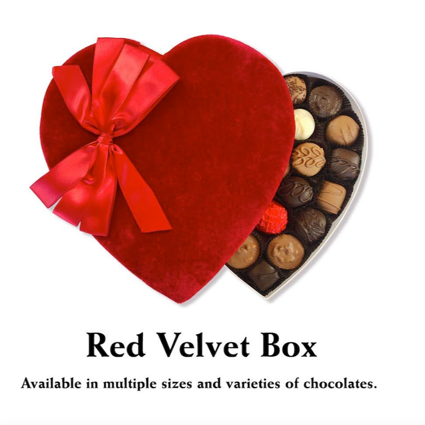 A Valentine's Day-themed Red Velvet Box featuring Florence’s Exquisite Chocolates in Rexburg, ID. This heart-shaped chocolate box is covered in plush red velvet fabric and adorned with a luxurious satin bow. Inside, an assortment of handcrafted chocolates, including milk, dark, and white varieties, are neatly arranged, showcasing their intricate designs and textures. The elegant presentation makes it an ideal romantic gift. The text below highlights that the Red Velvet Box is available in multiple sizes and chocolate assortments.