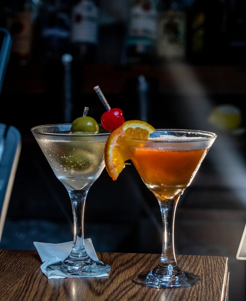 Handcrafted cocktails including a classic martini and a citrus-forward signature drink, garnished wi 