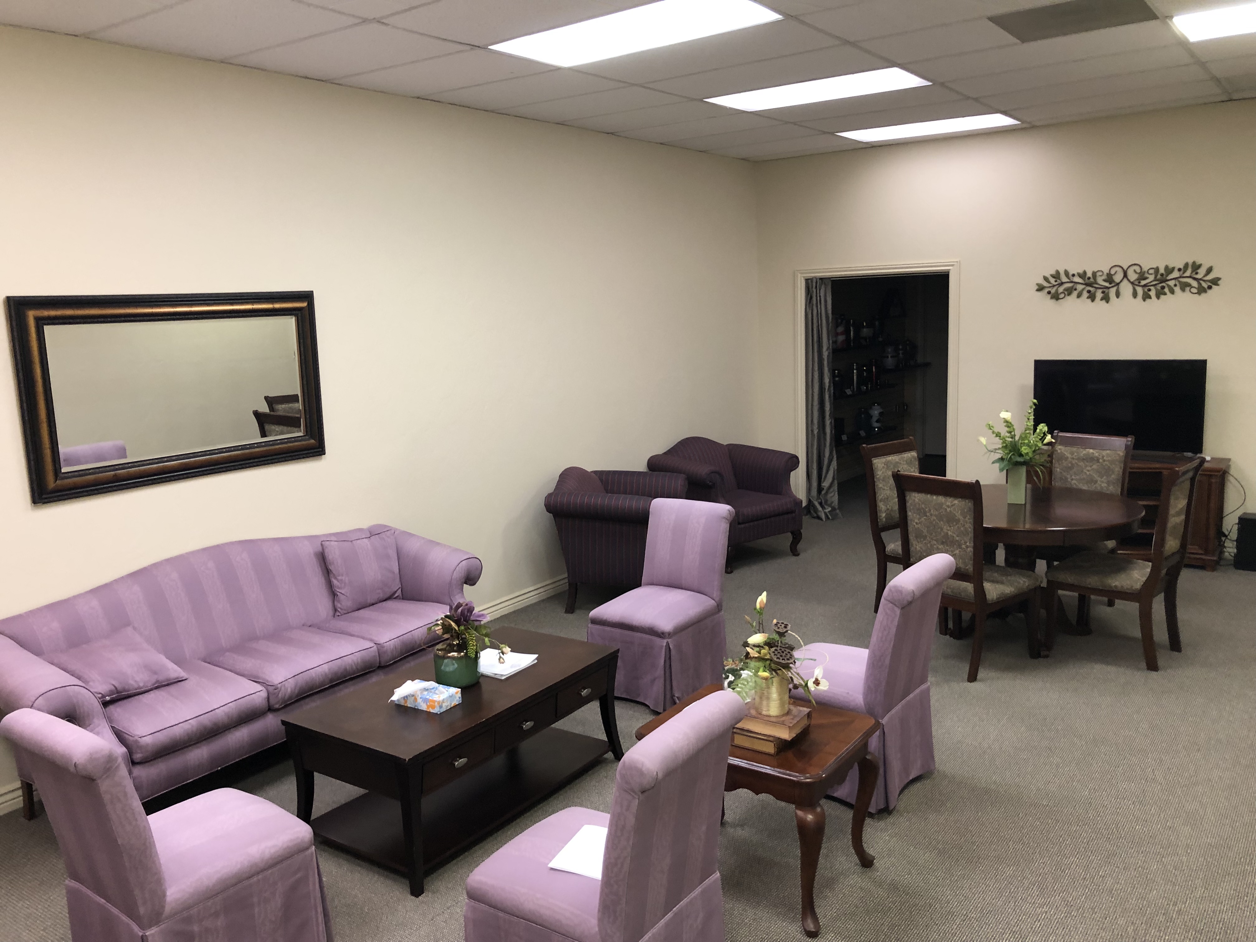 Family lounge with a mauve upholstered sofa and armchairs around a low wooden table, and a separate arrangement table with seating at the far end.
