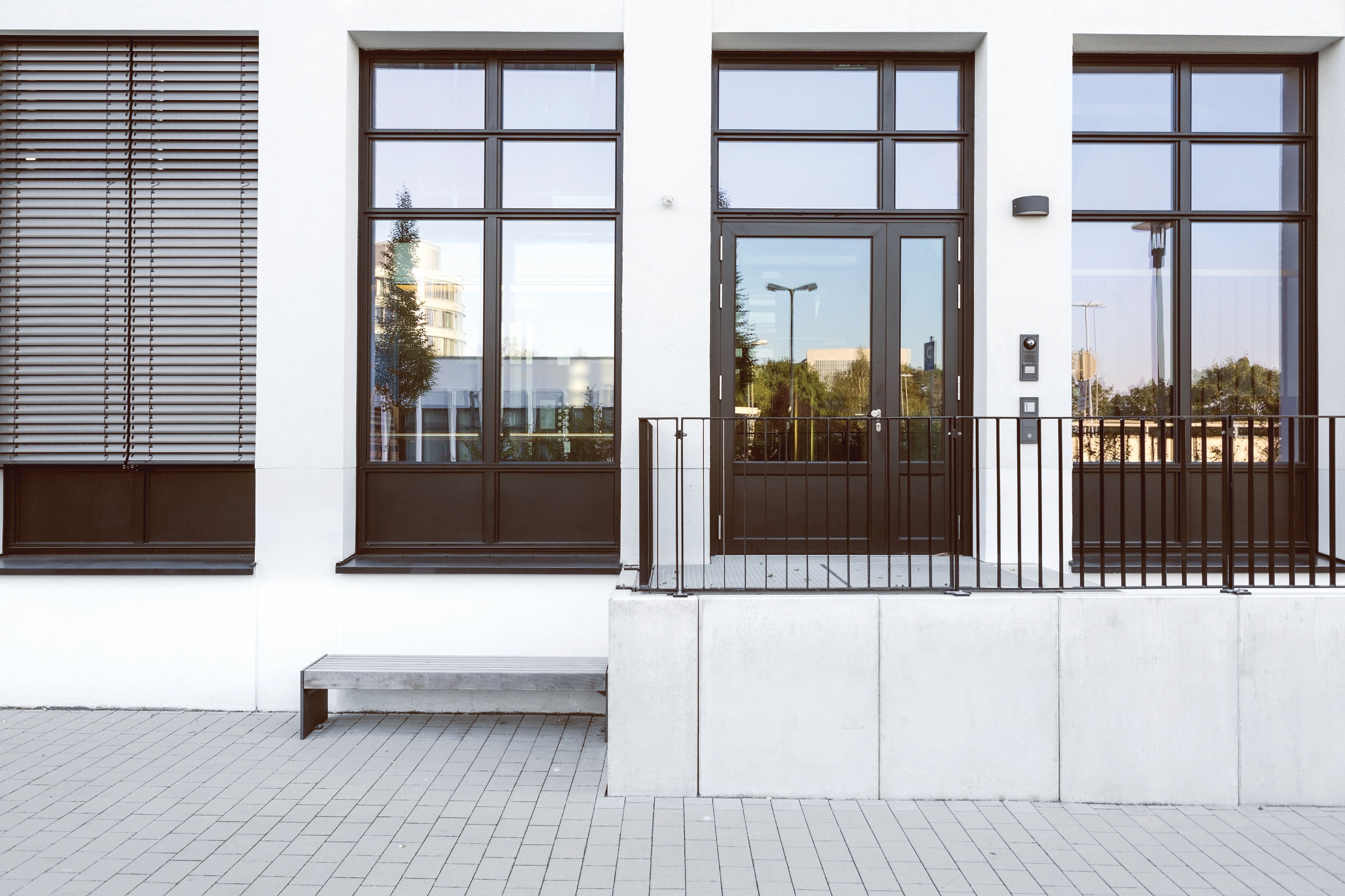 Tall, multi-pane windows next to a glass entry door on a modern white building exterior, emphasizing clean lines and vertical window design.