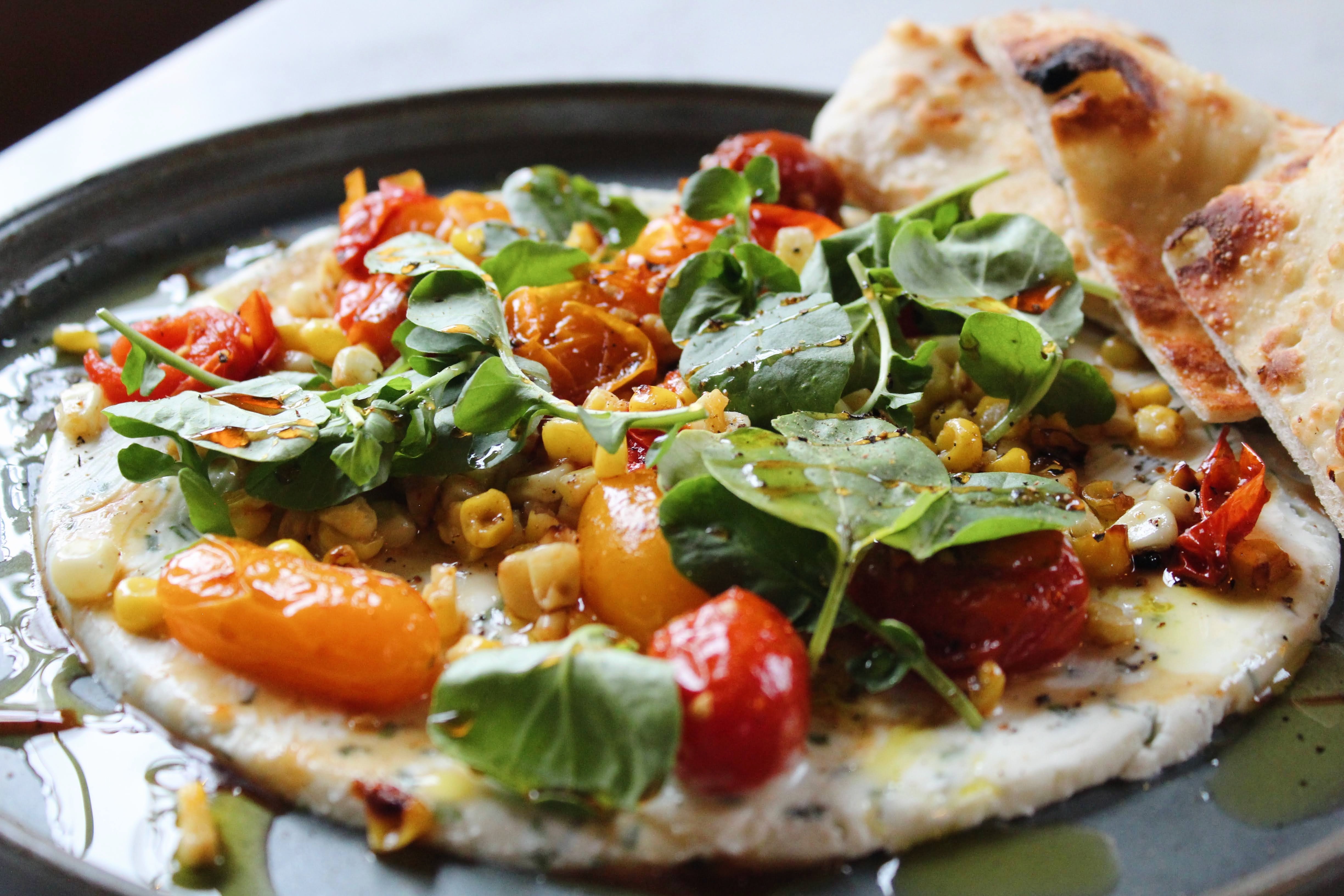 Ricotta Siciliana — creamy whipped ricotta piled with grilled corn, blistered cherry tomatoes, and fresh watercress, finished with balsamic reduction and served with warm flatbread.