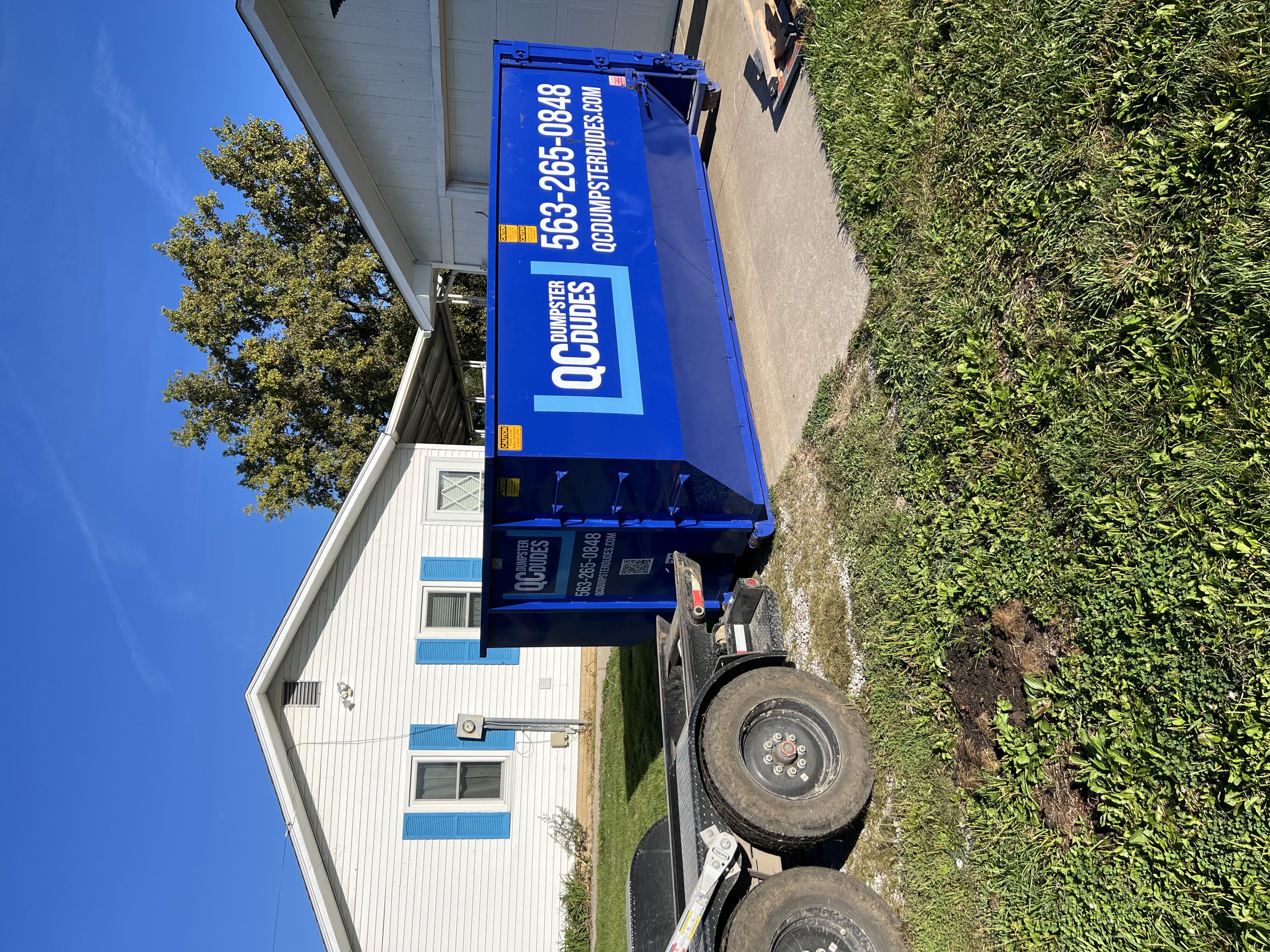 A QC Dumpster Dudes dumpster parked in a residential driveway, ready for cleanup or renovation projects.