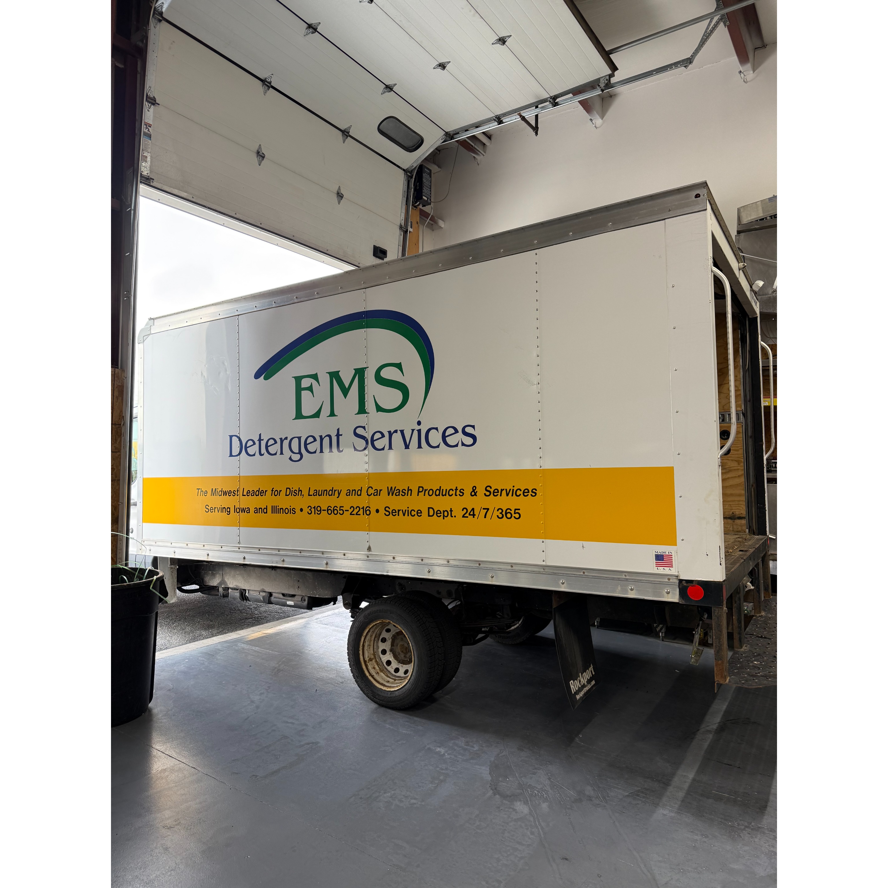 An EMS Detergent Services delivery truck is parked inside a warehouse bay, showcasing the company&rsquo;s branding and service coverage for dish, laundry, and car wash products across Iowa and Illinois.