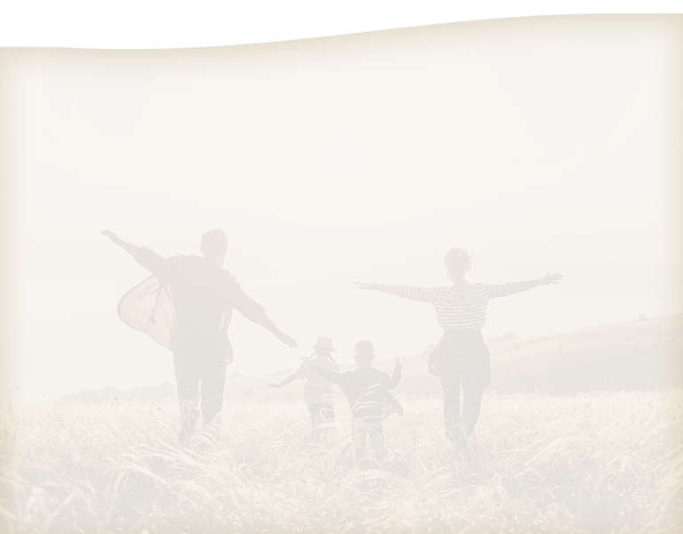 A young couple running through a field with their kids.