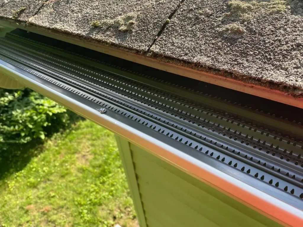 Close-up of a gutter guard system installed beneath roof shingles. Protective cover prevents debris  