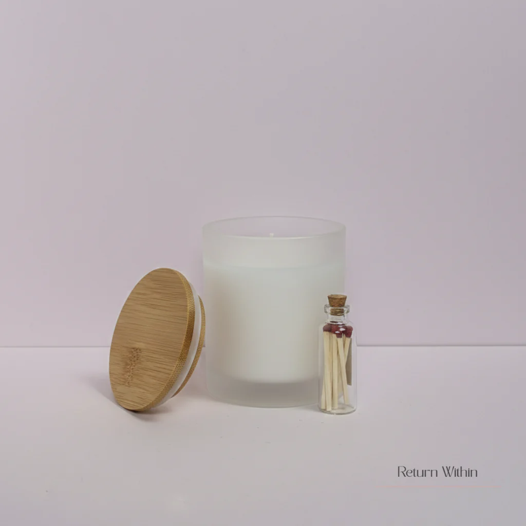 A white, frosted glass candle with a bamboo lid and a small glass bottle filled with matches sit on a light-colored surface. The background is a soft gradient of pale pink to white. The text "Return Within" is visible in the lower right corner.