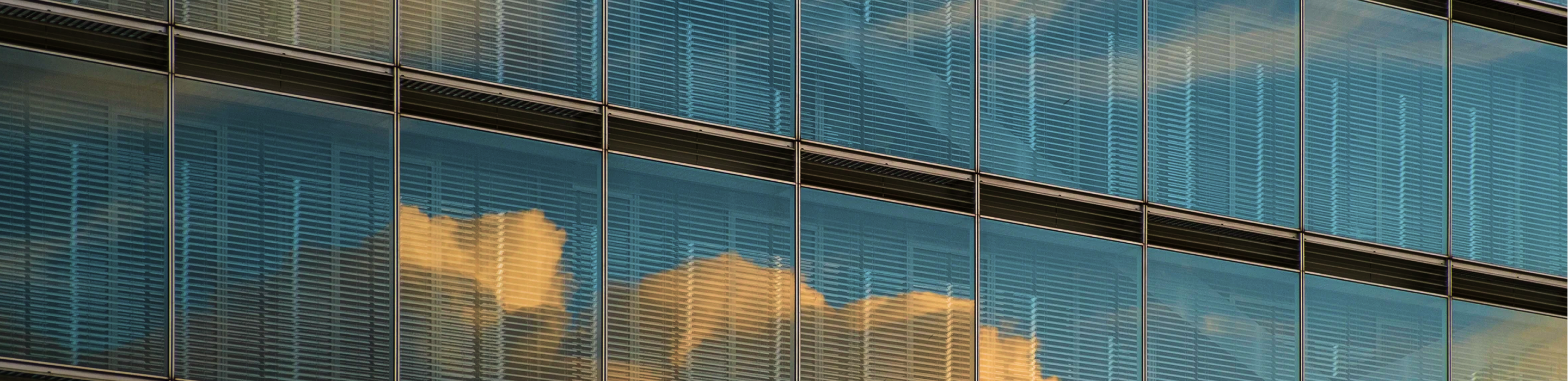 Close-up of a modern glass office building with clouds reflected in the windows.