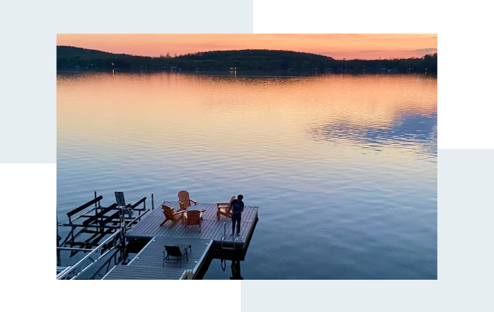 Person standing on a dock at sunset, enjoying the view of the lake.