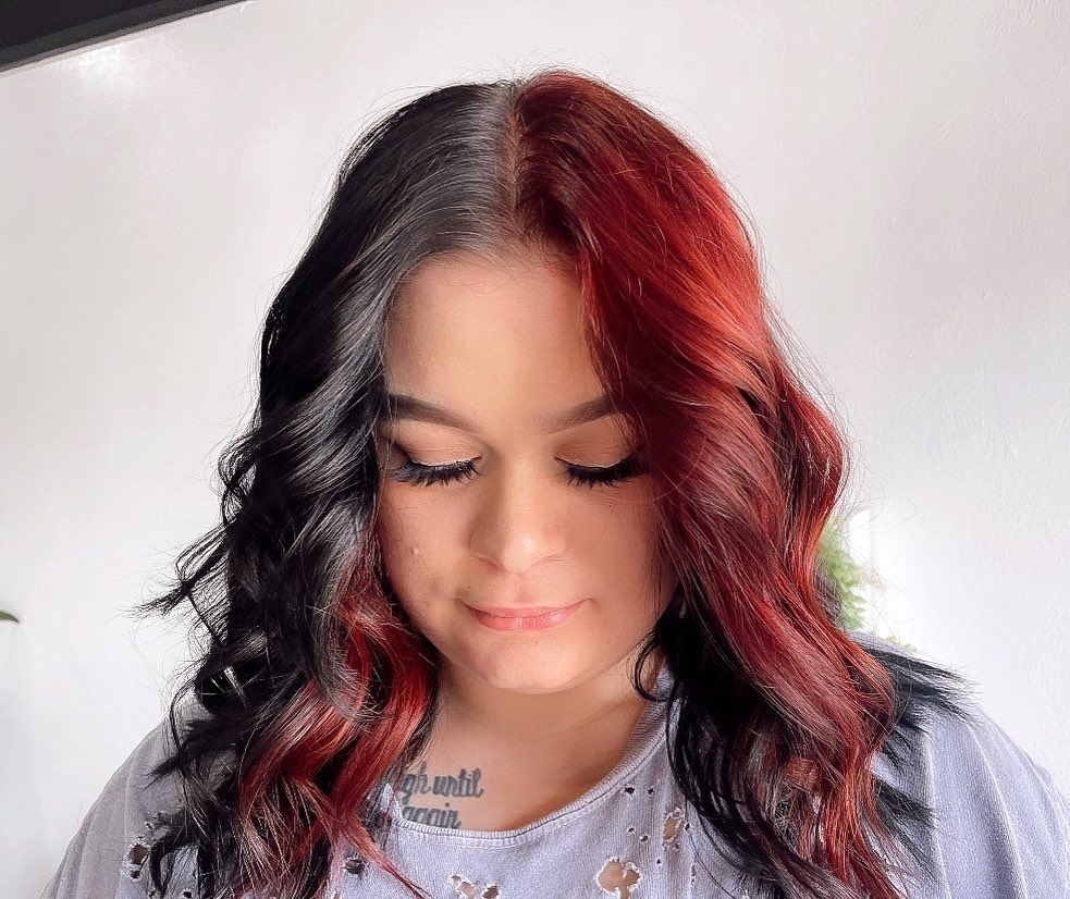 Woman with split-dyed hairstyle featuring black and deep red tones, styled in soft waves, showcasing a bold, modern salon hair color transformation.