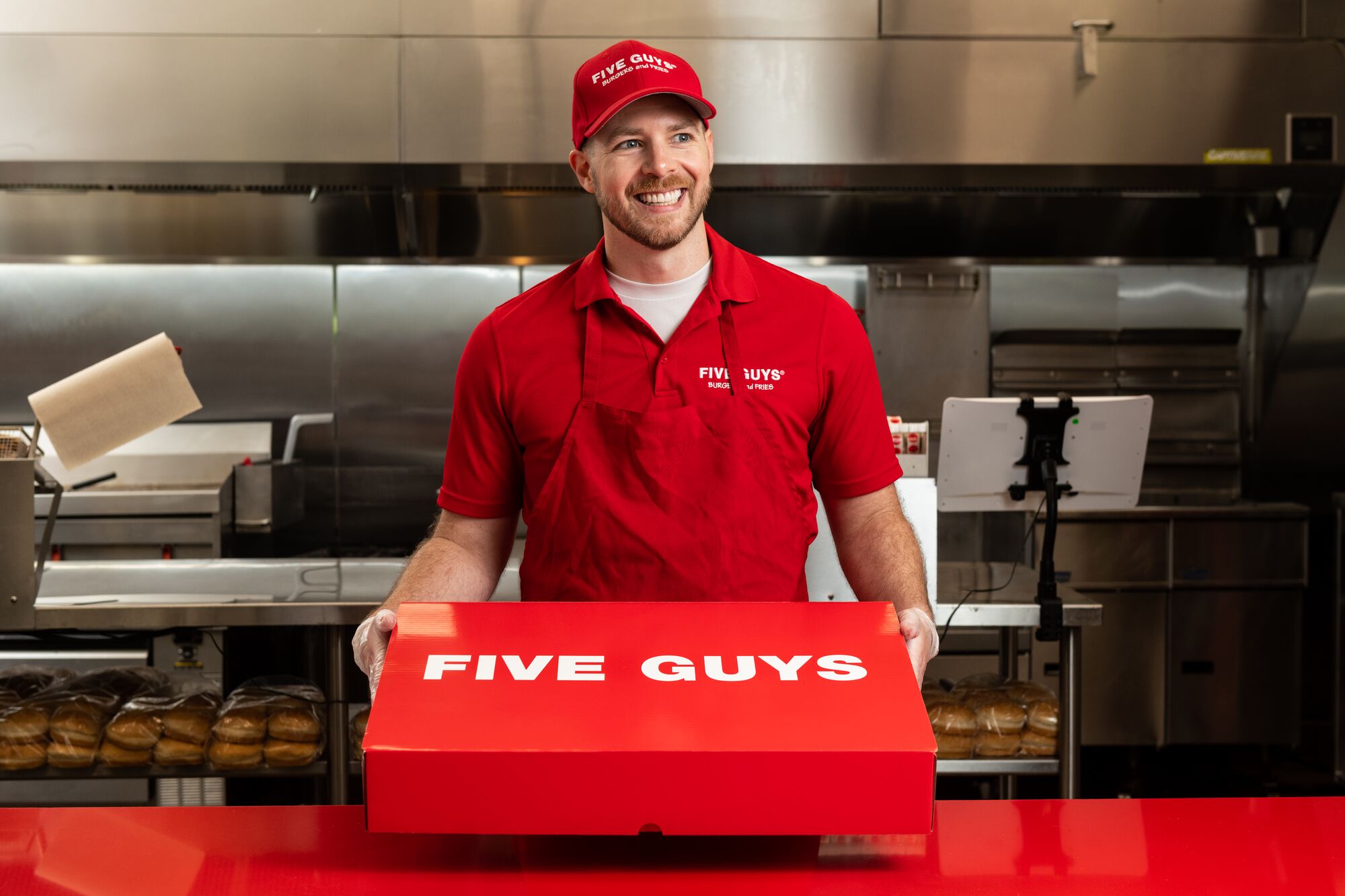 A Five Guys employee holds the red Five Guys catering box at the counter.