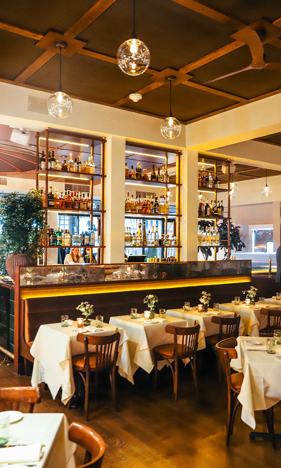 A wide view of the restaurant's sophisticated interior showing glowing globe lights, a fully stocked back bar, and neatly set dining tables.