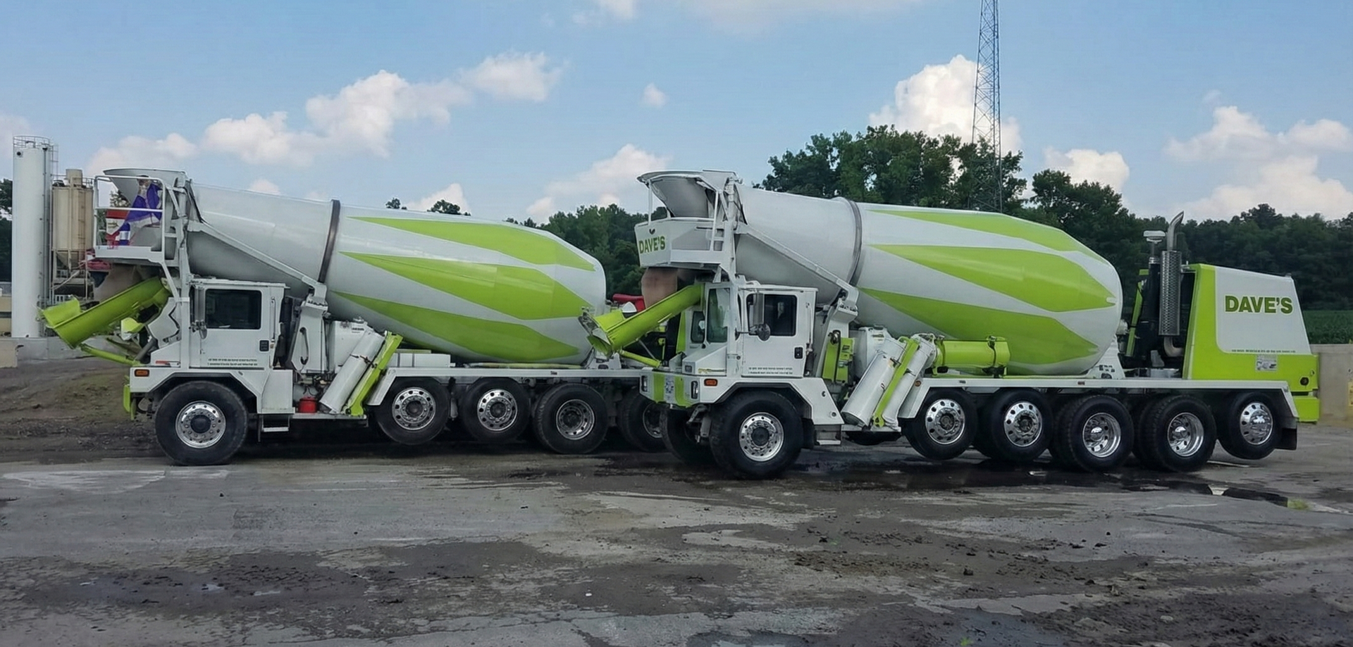 Two professional Dave&rsquo;s Concrete mixer trucks, featuring their signature lime-green and white striped drums, are parked side-by-side on a damp industrial lot under a clear blue sky.