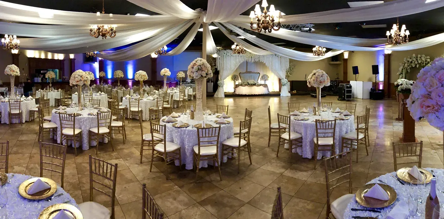 Beautiful wedding reception venue featuring ceiling drapery, gold chairs, floral centerpieces, elega 