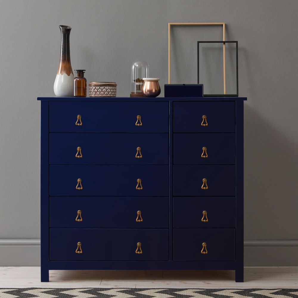 A navy blue painted chest of drawers in front of a dark grey wall.