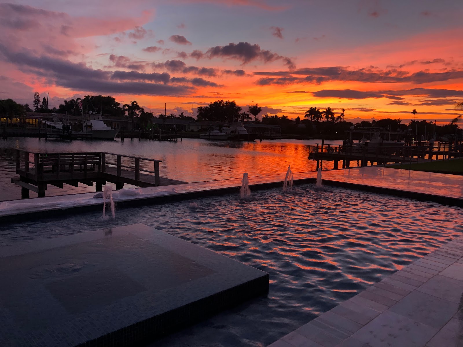 Modern waterfront swimming pool at sunset with illuminated water features, dramatic skies, and a relaxing outdoor setting.