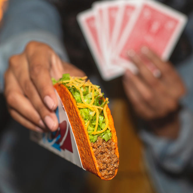 Une personne tenant des cartes à jouer rouges dans une main et offrant un Loco Taco Taco Bell Doritos® avec l'autre.