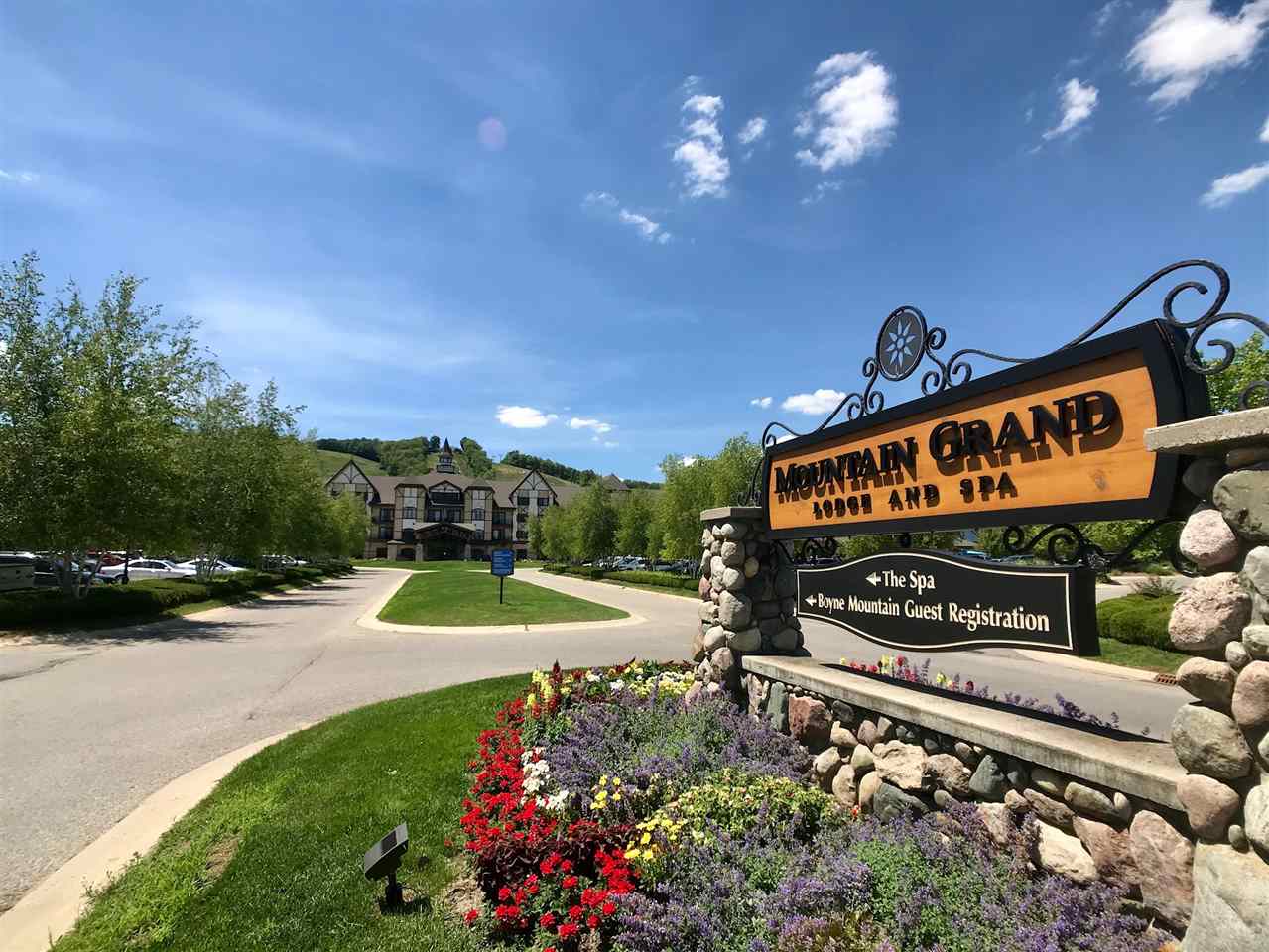 A sign for Mountain Grand Lodge and Spa with directions to The Spa and Boyne Mountain Guest Registration stands in front of a large lodge-style building, surrounded by trees and landscaping.