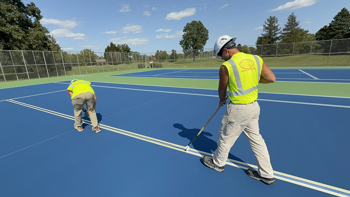 2 PLM workers painting lines on a new tennis court.