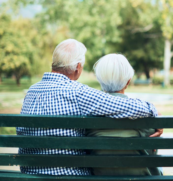 An elderly couple sitting together on a park bench.
