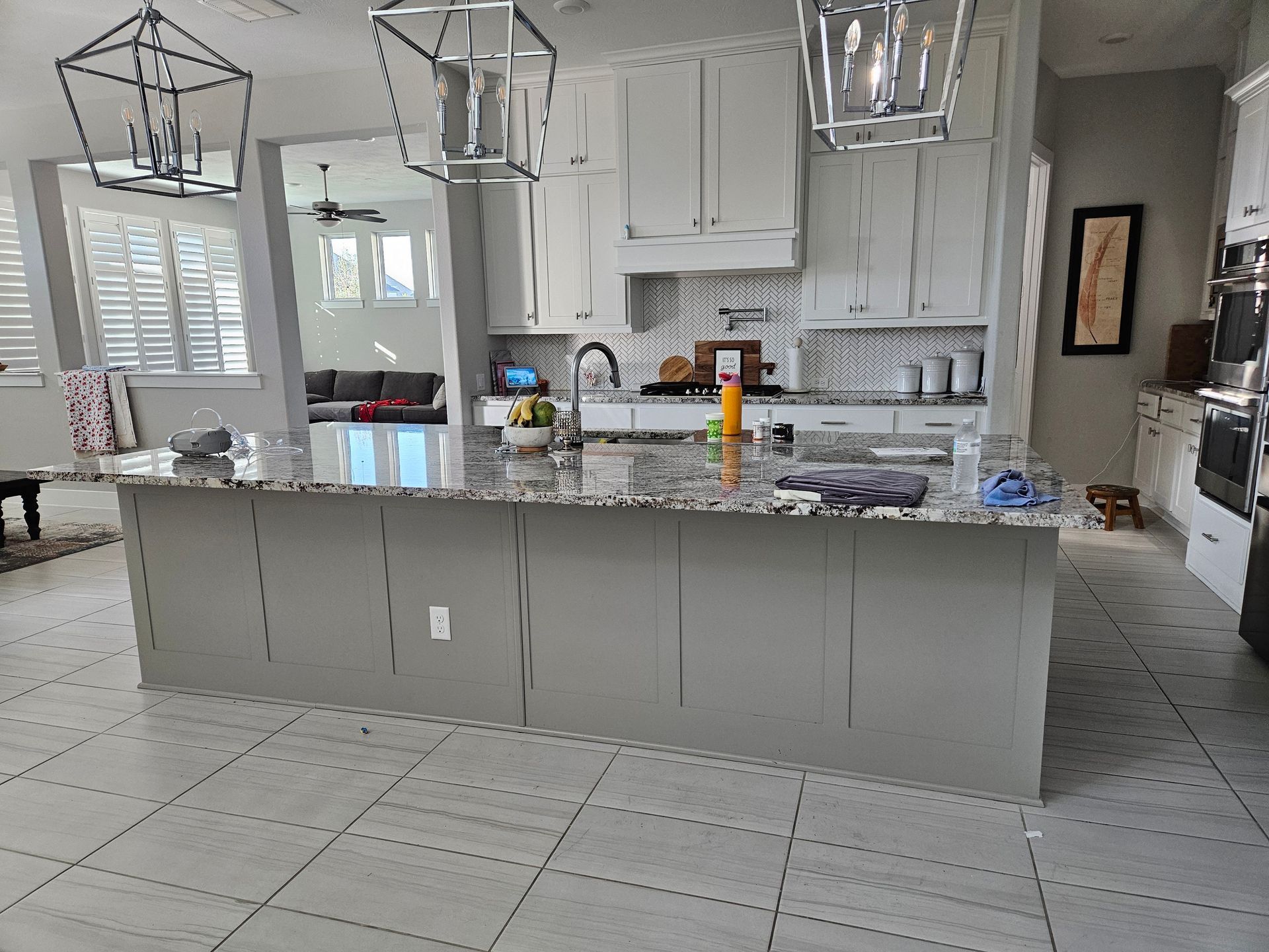 Luxury kitchen featuring professionally painted white cabinetry, large granite island, decorative lantern pendants, patterned backsplash, and premium finishes, delivering timeless elegance with exceptional residential painting craftsmanship throughout.