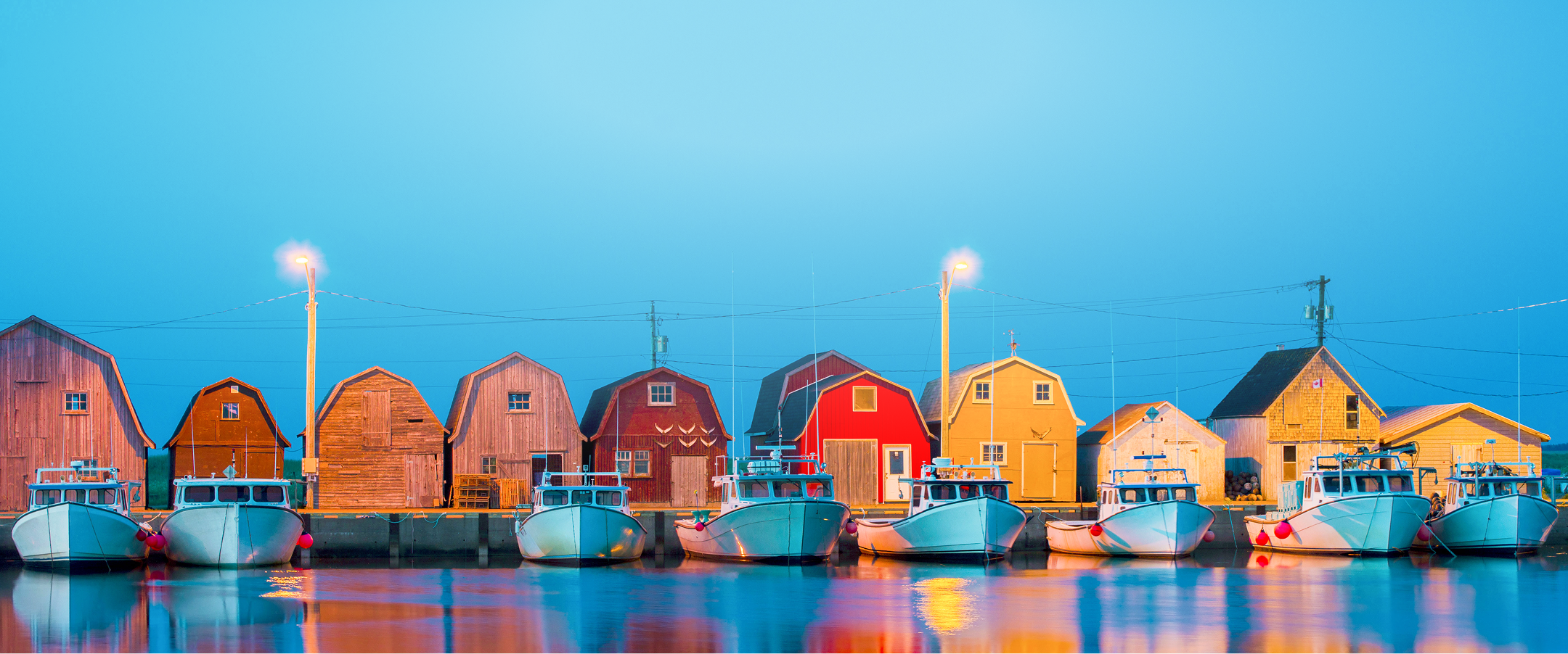 Charming row of docked fishing boats and fishing sheds during blue hour at Malpeque Harbour, Prince Edward Island.