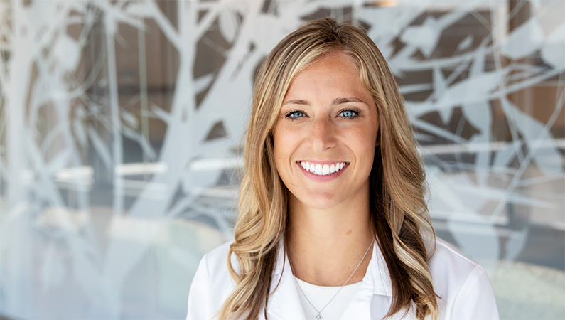 Woman smiling in front of a clear wall with a white tree decal.