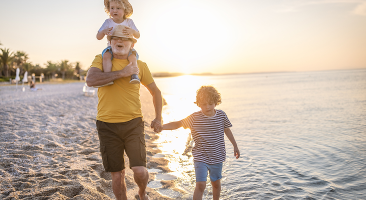 A grandfather walking along the beach with his two young grandchildren at sunset.
