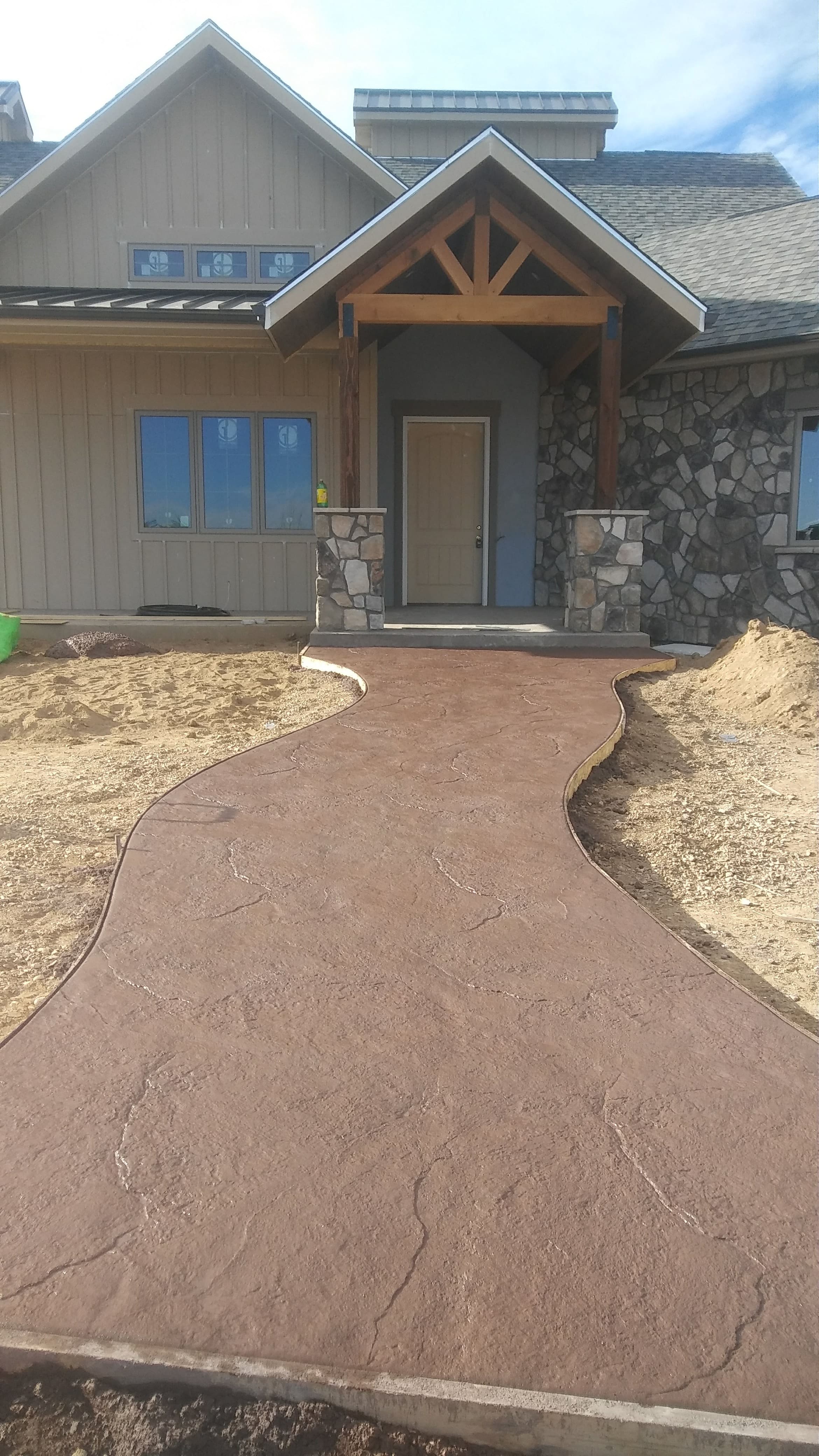 Decorative stamped concrete walkway leading to a residential entryway, featuring a warm earth-tone finish and natural stone texture with curved edges.
