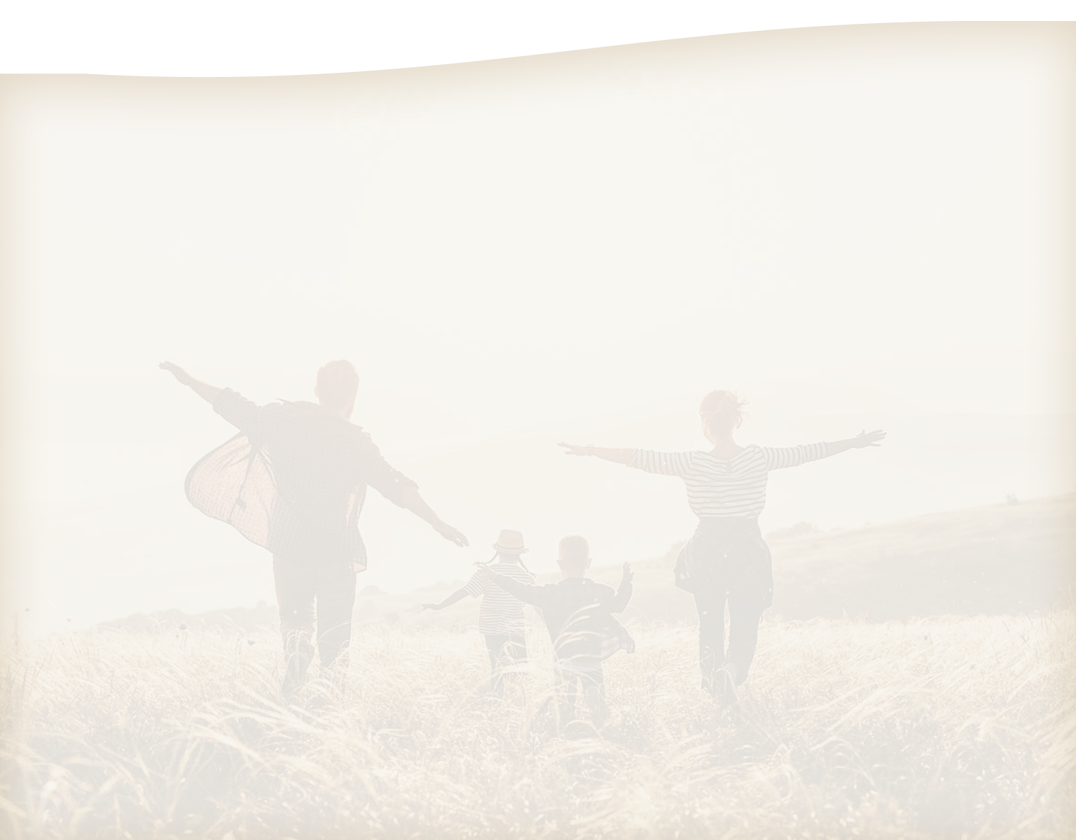 A young couple running through a field with their kids.