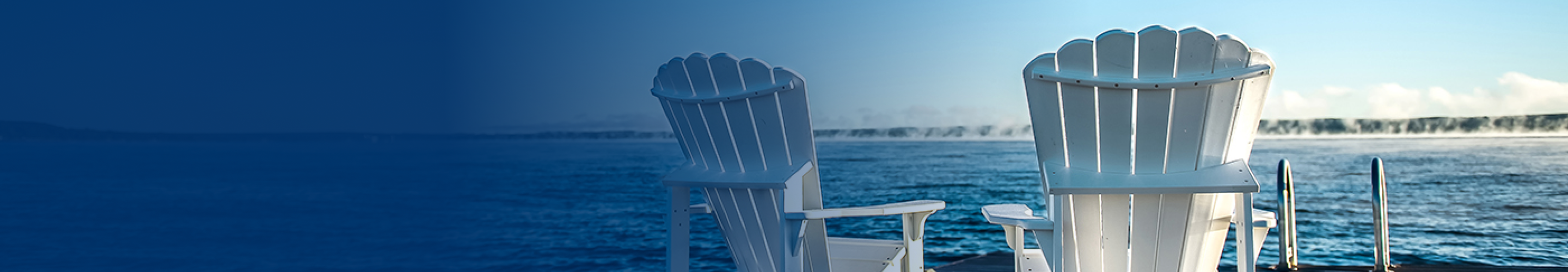 Two white Muskoka chairs on a dock facing towards a lake.