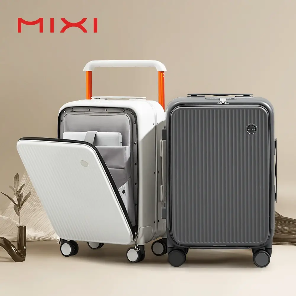 Two MIXI brand suitcases, one white and one grey, are displayed against a neutral background. The white suitcase is open, revealing its organized interior with compartments for a laptop and other items. The grey suitcase is closed, showcasing its ribbed exterior. Both suitcases have orange accents on their retractable handles. A small decorative plant in a modern vase is visible to the left, and a textured element resembling fabric or wood is on the right.