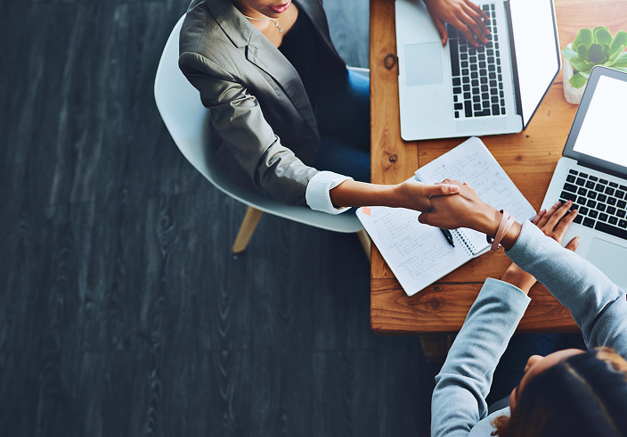 Top-down view of two people shaking hands during a meeting.