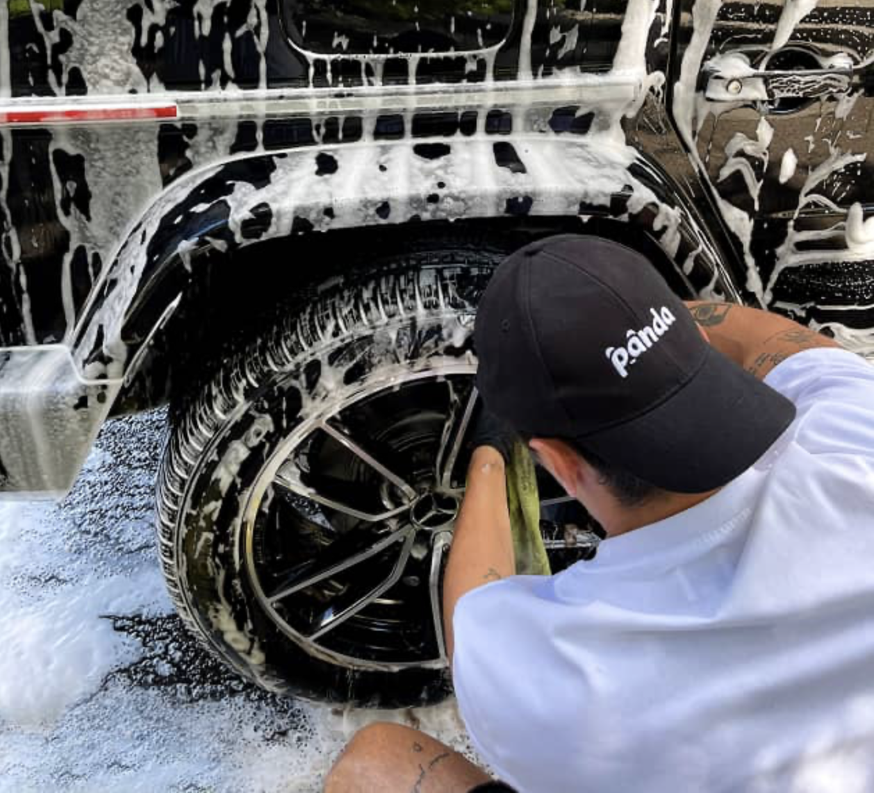Professional mobile car detailing expert cleaning the front grille of a black luxury SUV.