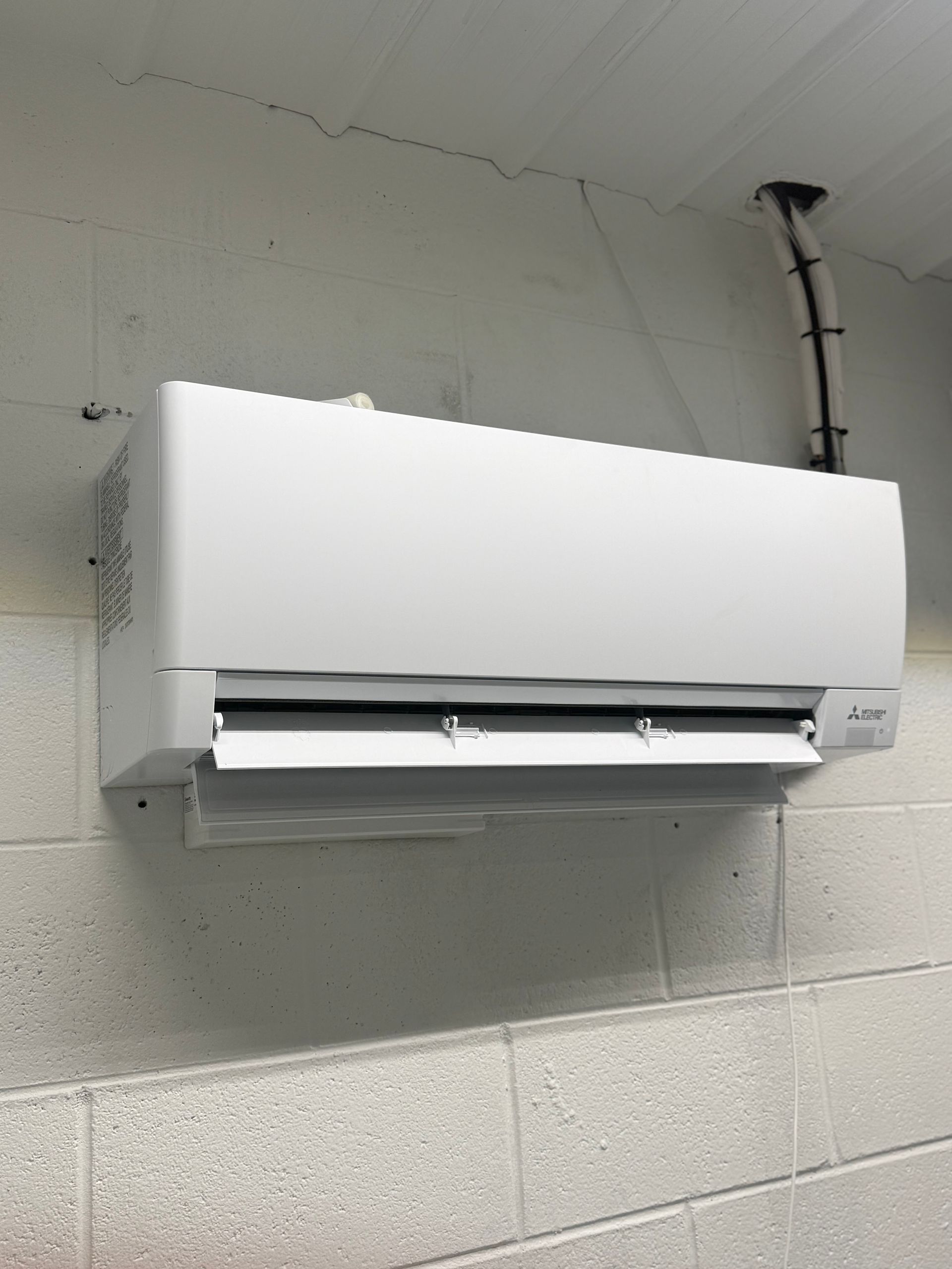 White Mitsubishi Electric wall mounted mini split indoor unit installed on a painted block wall, fea 