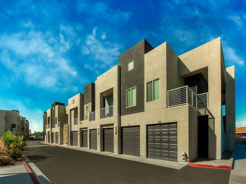 Exterior view of a building with beige and dark grey walls. There is a blue sky.