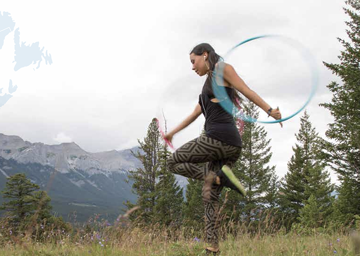 A woman performing a Hoop Dance with mountains in the background.