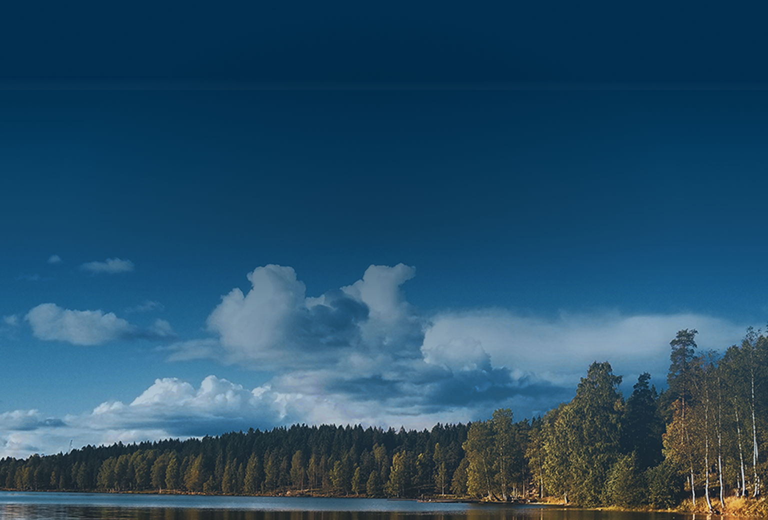 A calm lake surrounded by trees on a partly sunny day.