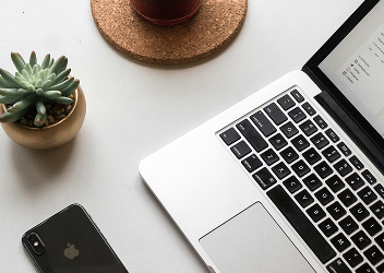 Close-up of an open laptop, a cell phone, and a succulent on a desk.