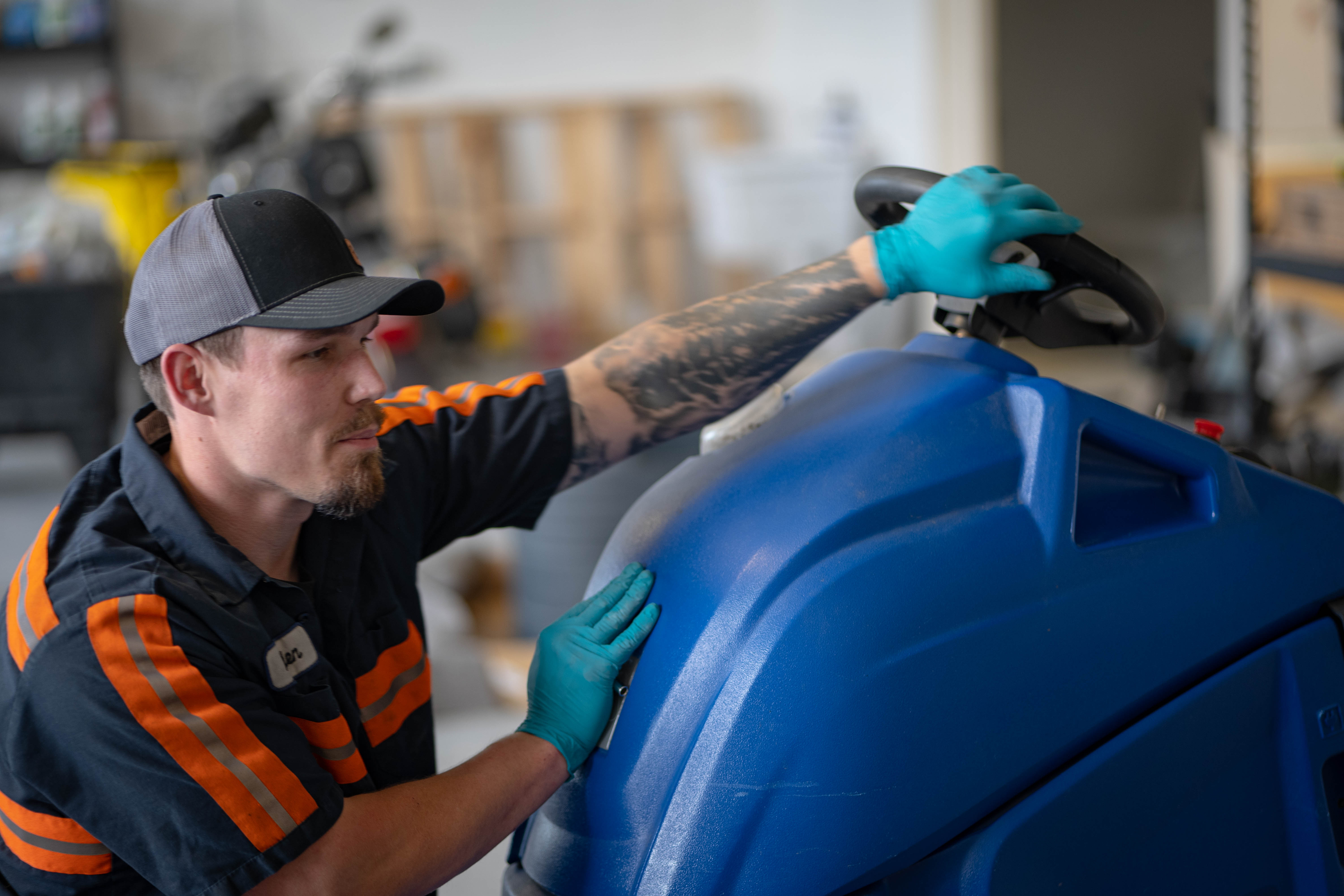 A WaySolutions technician in a high-visibility uniform inspects the steering wheel and upper control housing of a blue commercial floor scrubber. Providing expert fleet maintenance in Layton, Utah, our team ensures precise operator control and safety for commercial cleaning equipment.