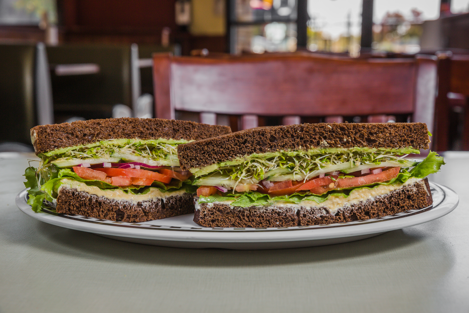 Veggie sandwich served on Pumpernickel bread with hummus, cream cheese, avocado, lettuce, tomato, onion, cucumber, and sprouts