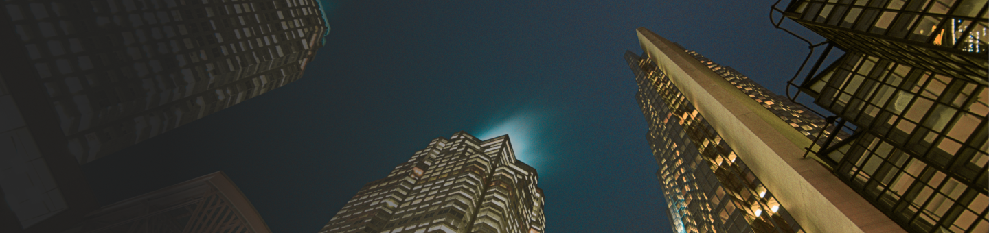 Upward view of several large skyscrapers at night.