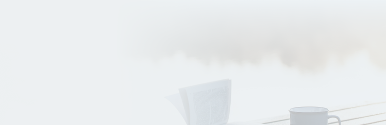 An open book next to a coffee mug on an outdoor table.