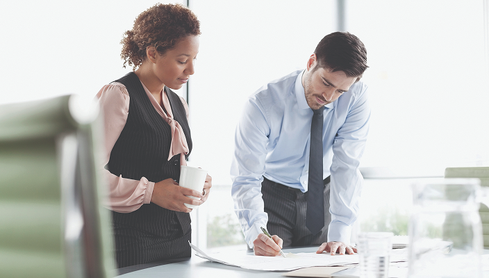 Two professionals reviewing documents together in a bright boardroom.