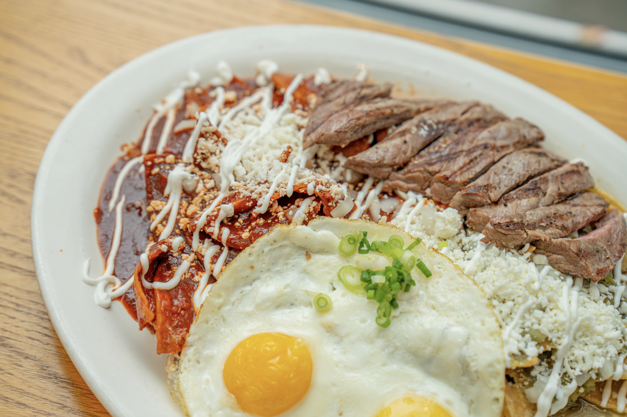 A chilaquiles plate with 2 fried eggs, a carne asada steak, and red sauce chilaquiles