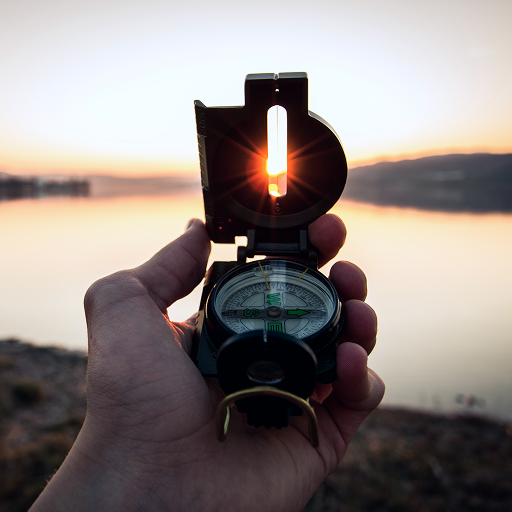 A person holding a compass in the direction of the sunset.