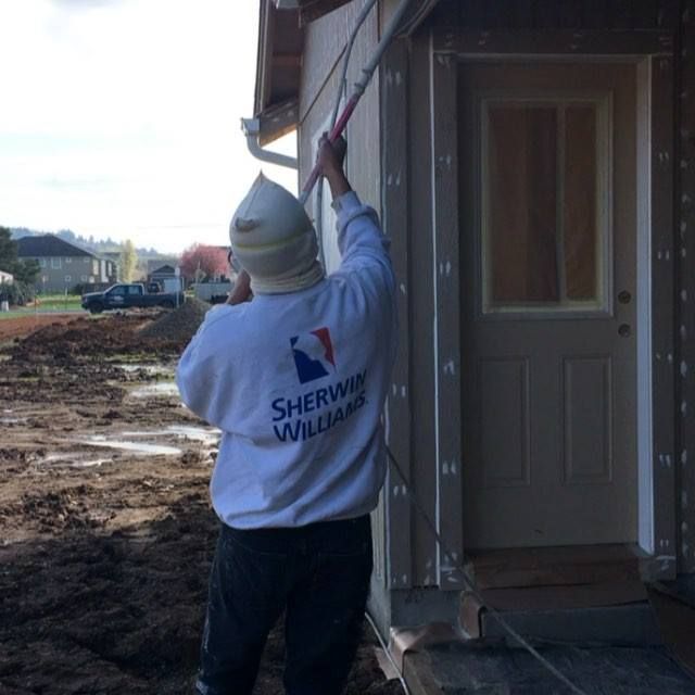 Contractor painting exterior siding of residential property, applying protective coatings that impro 